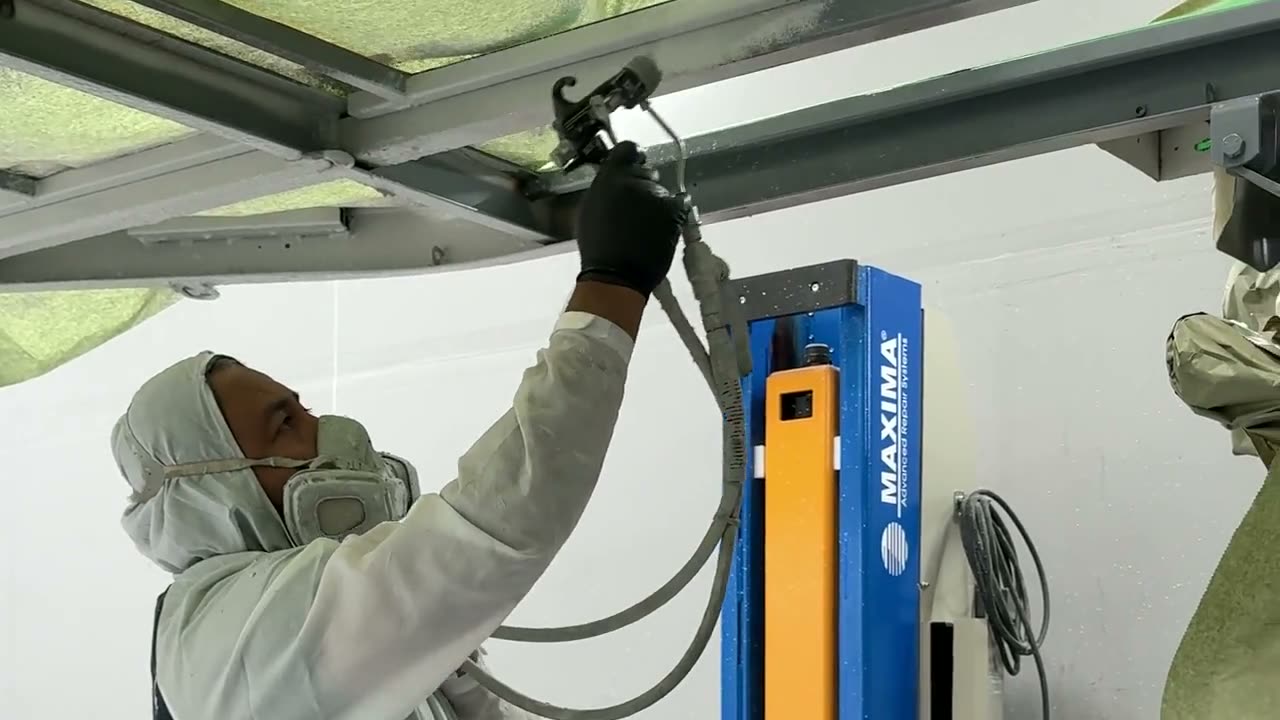 Technician applying protective undercoating to a motorcoach frame at the shop