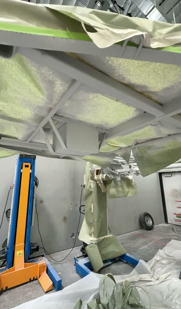 Close view of masked and coated structural surfaces beneath a motorcoach in the shop